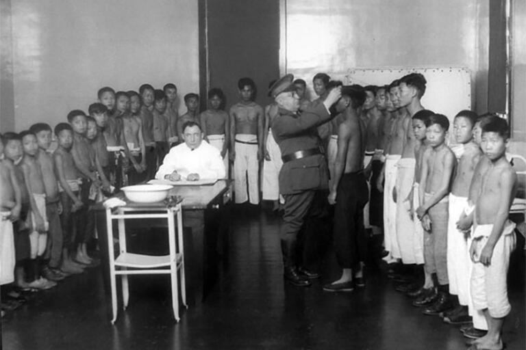 A group of Asian immigrants are given exams by medical staff at Angel Island Immigration Station in the early 20th century.