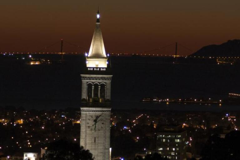 Night photo of the Campanile with the Golden Gate Bridge in the background. 
