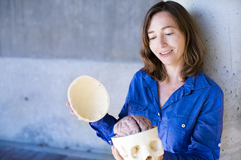 Portrait of Professor SIlvia Bunge, Dept. of Psychology, holding a plastic skull with a model of a brain inside. 