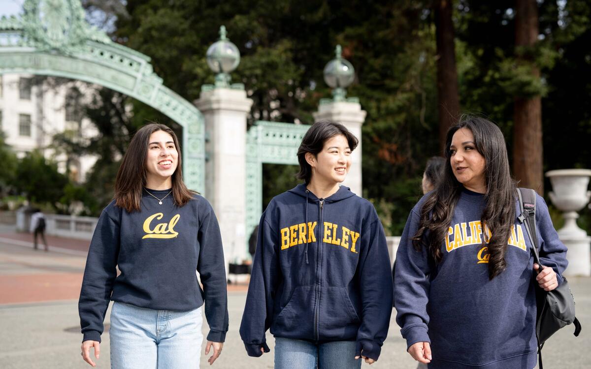 3 students smiling walking in front of sather gate