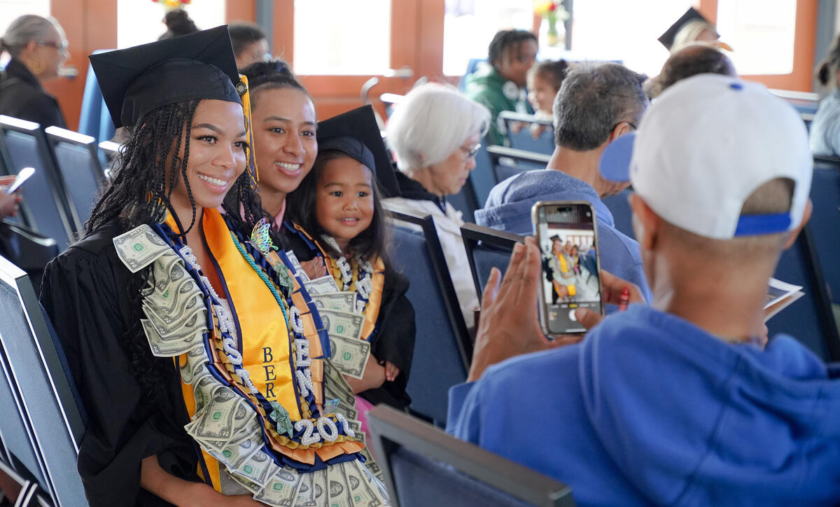 A graduate in regalia with two younger family members posing and smiling for a camera