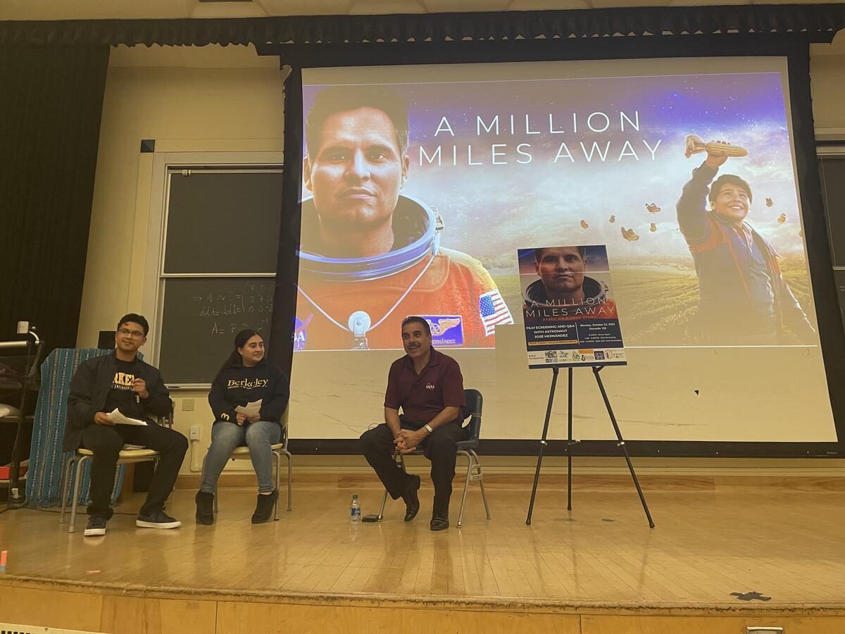 Three people are on stage (two moderators) along with engineer and UC Regent José Hernández. Behind them is a screen with the text “A Million Miles Away.”