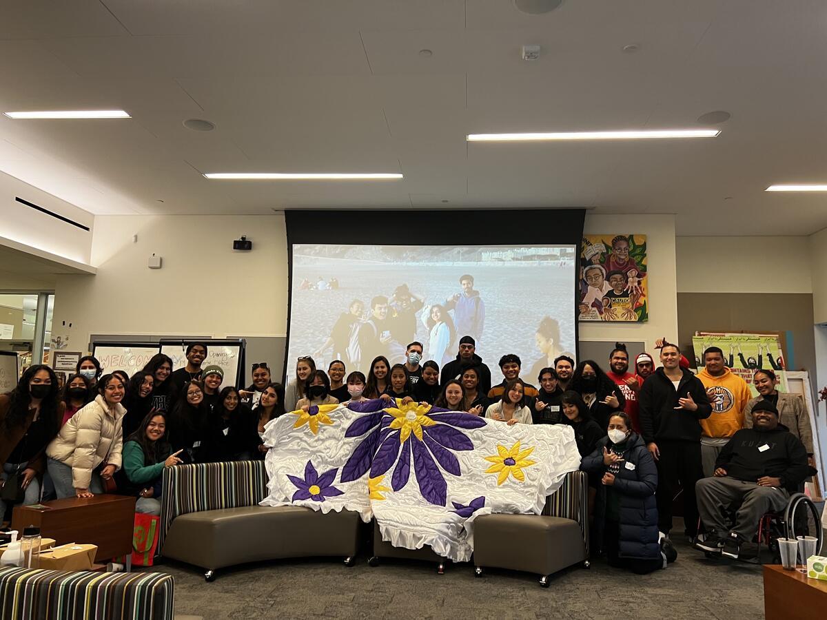 A group of students indoors holding up a white, purple, and yellow fabric