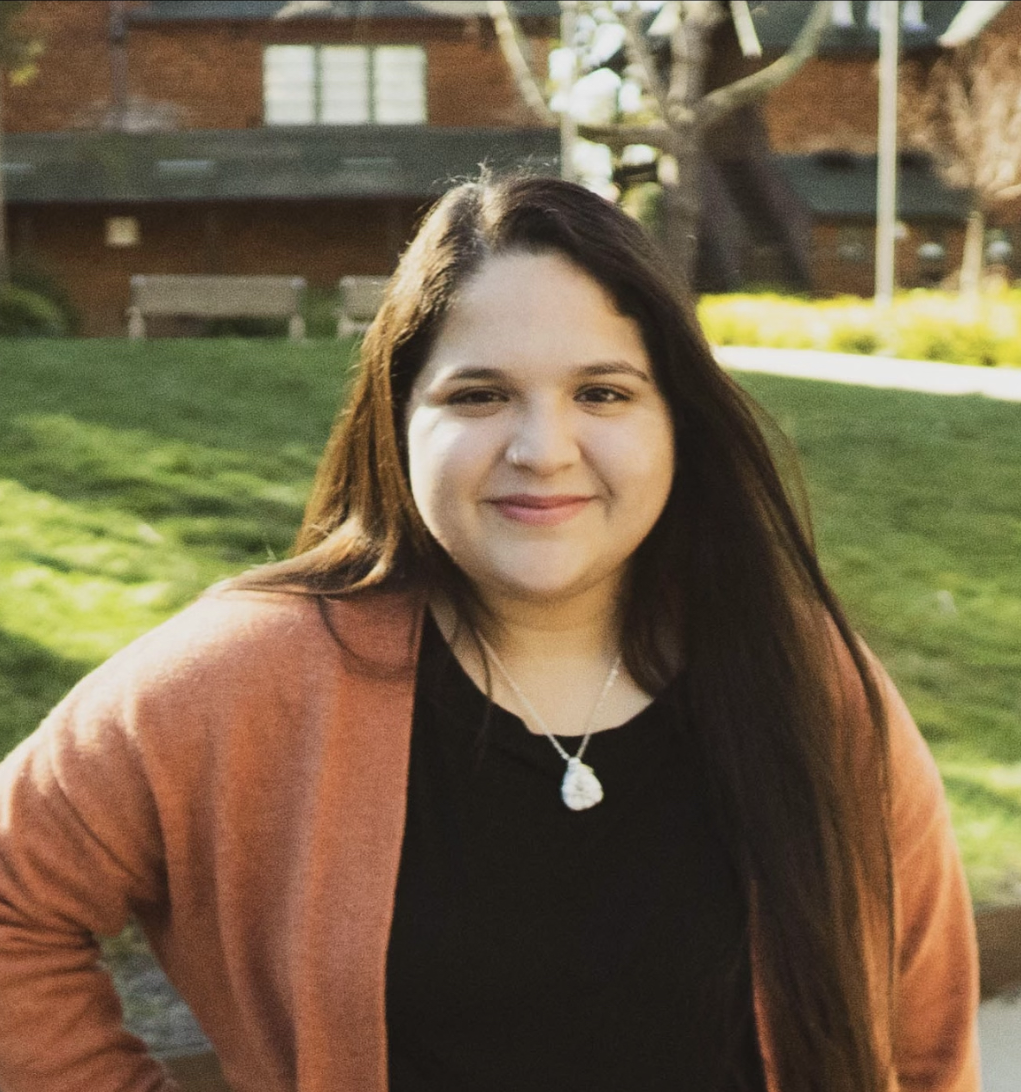 Headshot of Denise Mendez wearing an orange sweater and black t-shirt underneath.