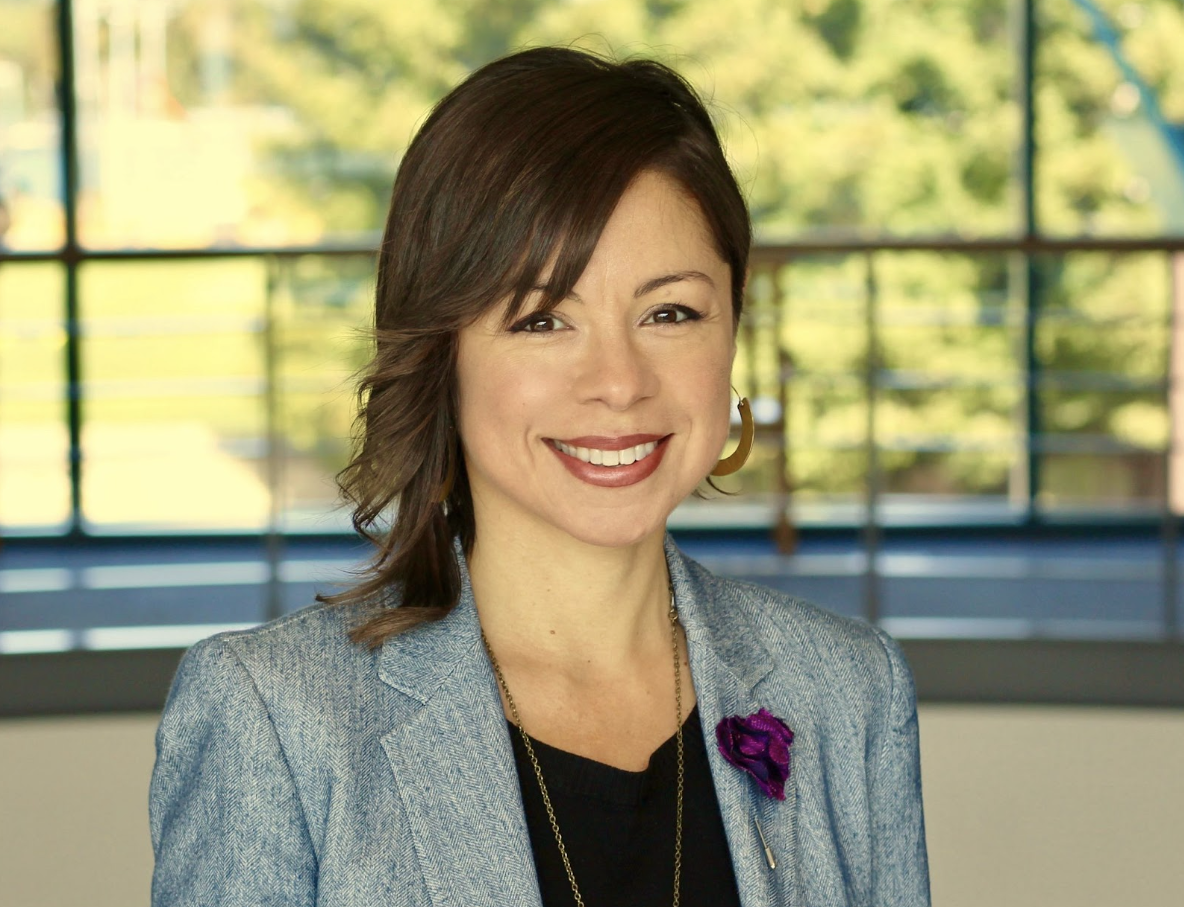 Diana Peña, PhD wearing a grey blazer with a forest background behind her.