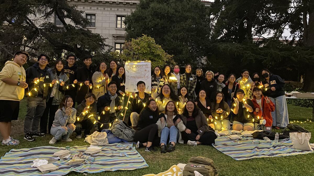 A group of students gathered on the grass holding up a string of lights