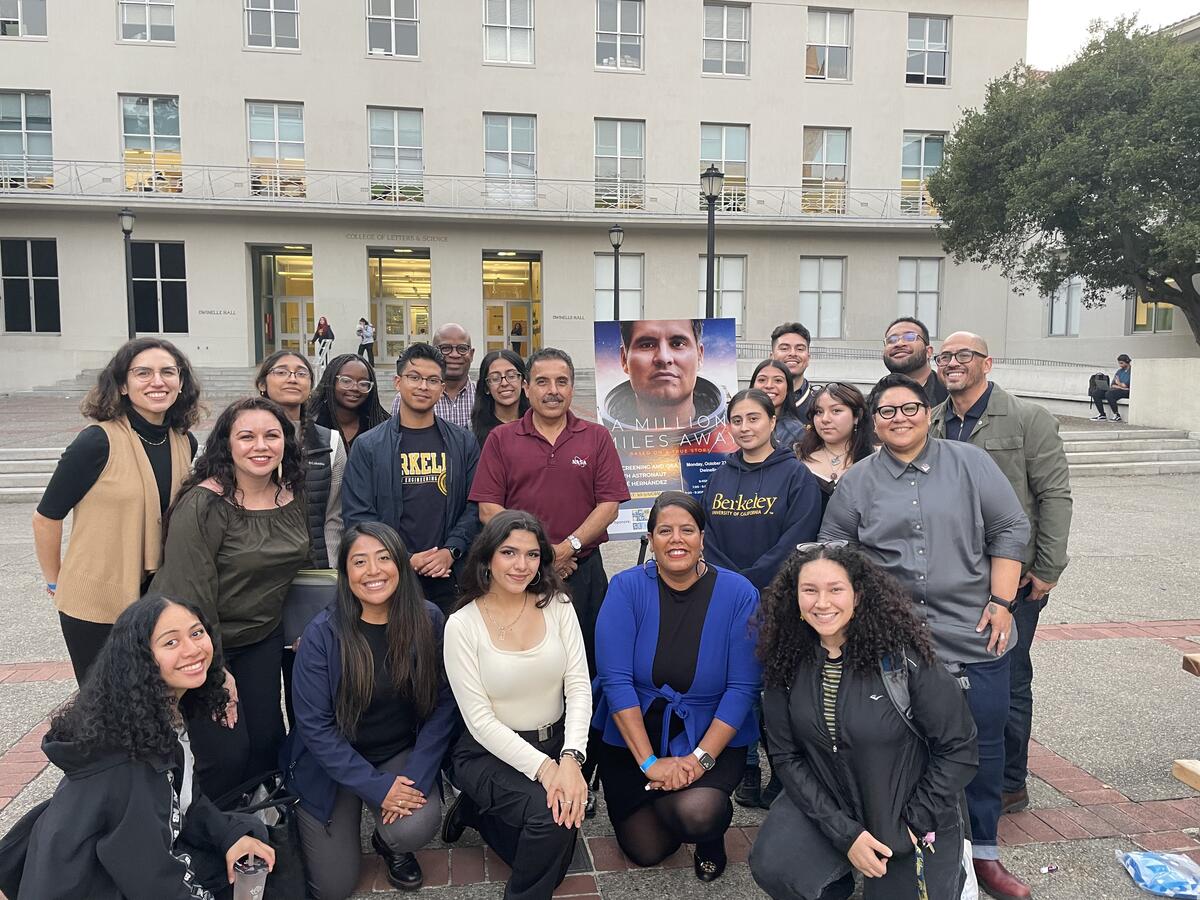 Twenty people standing in front of a building with the event flier on a poster board reading: A Million Miles Away. At the center is UC Regent José Hernández.