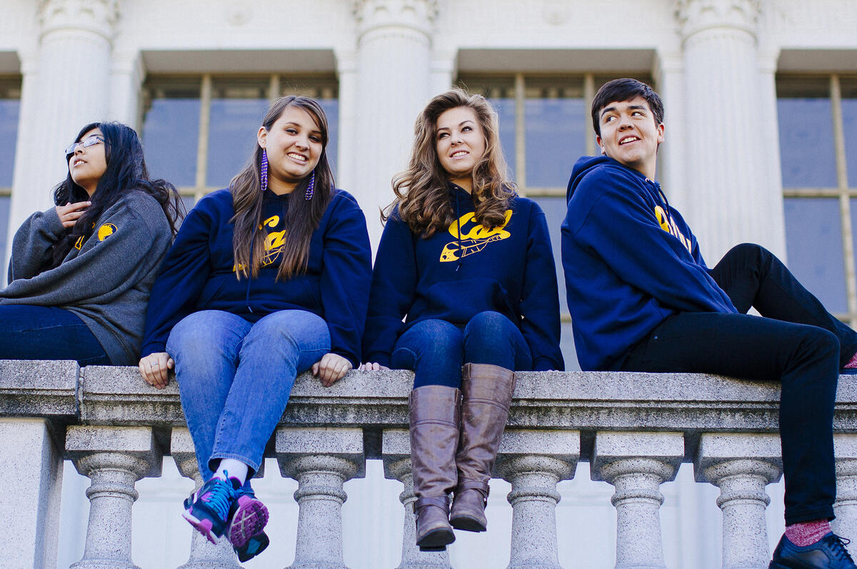 4 students wearing Cal hoodies sitting in front of Doe library smiling