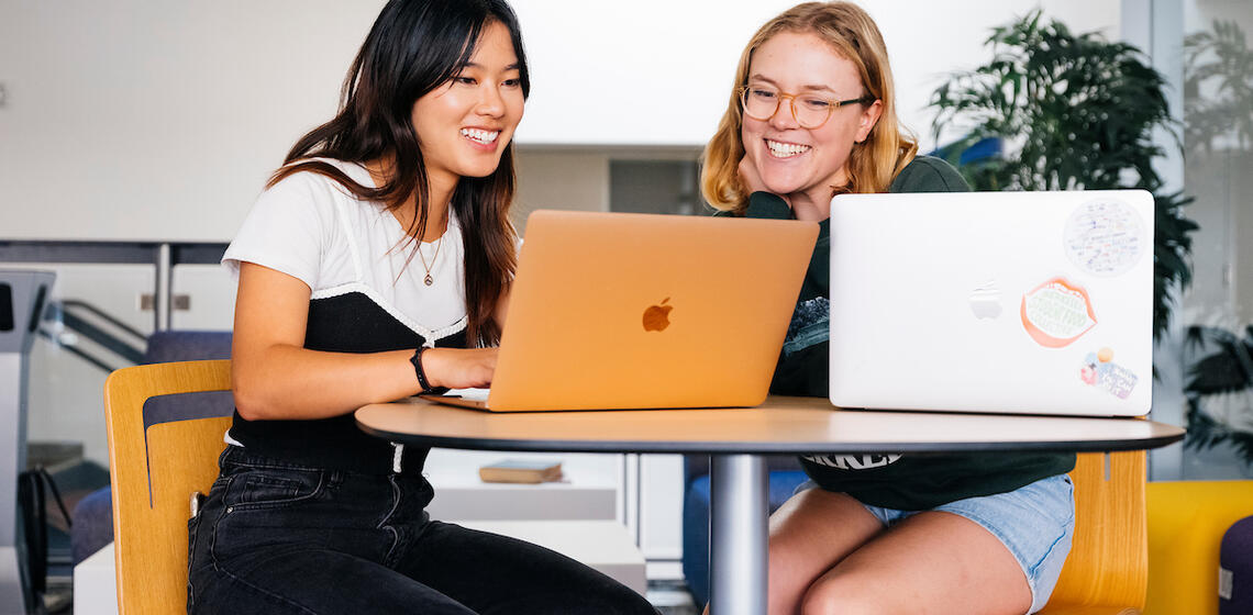 two people working on their laptop on a desk smiling at the career center