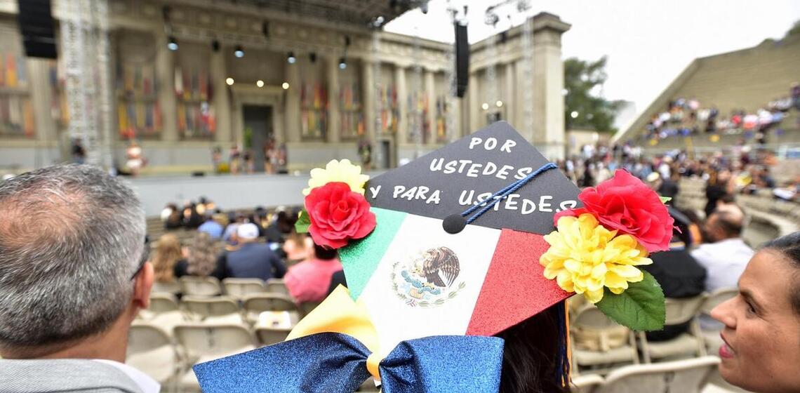 A graduate wears a cap that says, “Por ustedes y para ustedes,” or “For you and for you.”