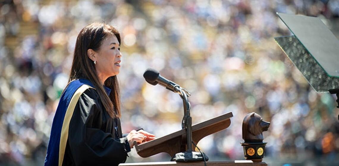 sunny lee, wearing a cap and gown, talks at a podium during a sunny graduation event