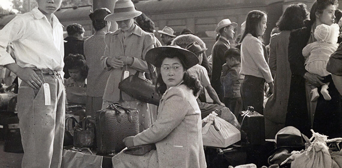 Families of Japanese ancestry wait with their belongings for a train to take them to the Merced Assembly Center.